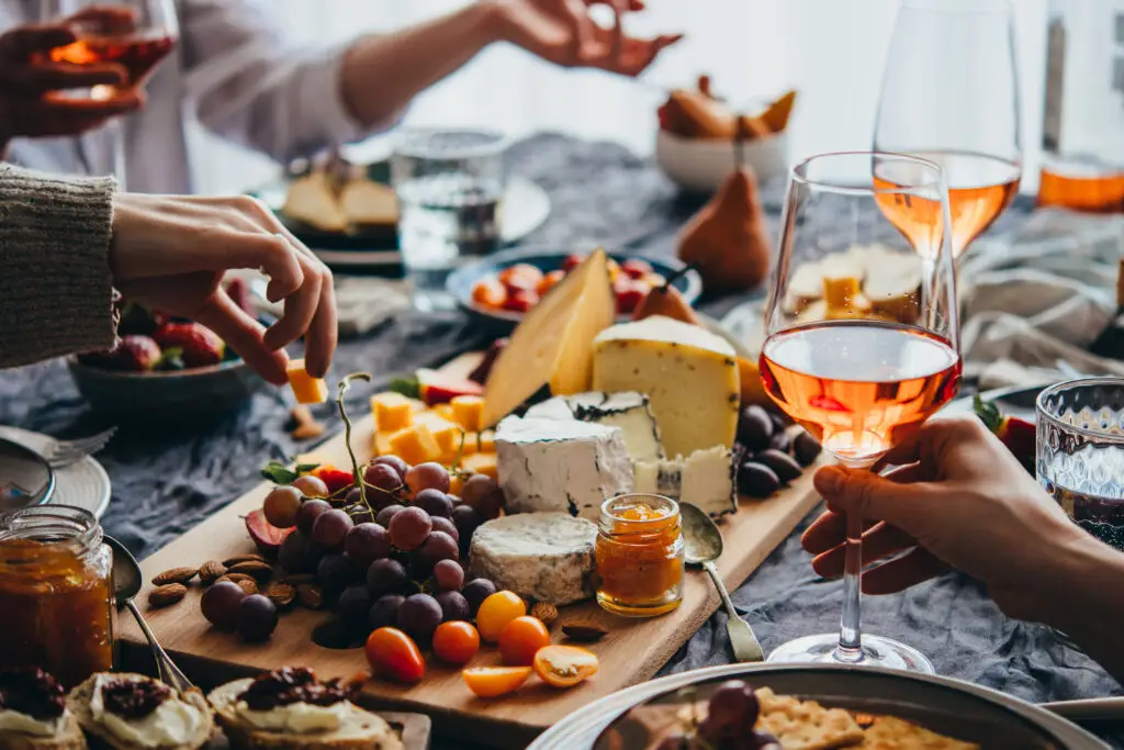 Friends enjoying dinner party with different kinds of appetizers and rose wine
