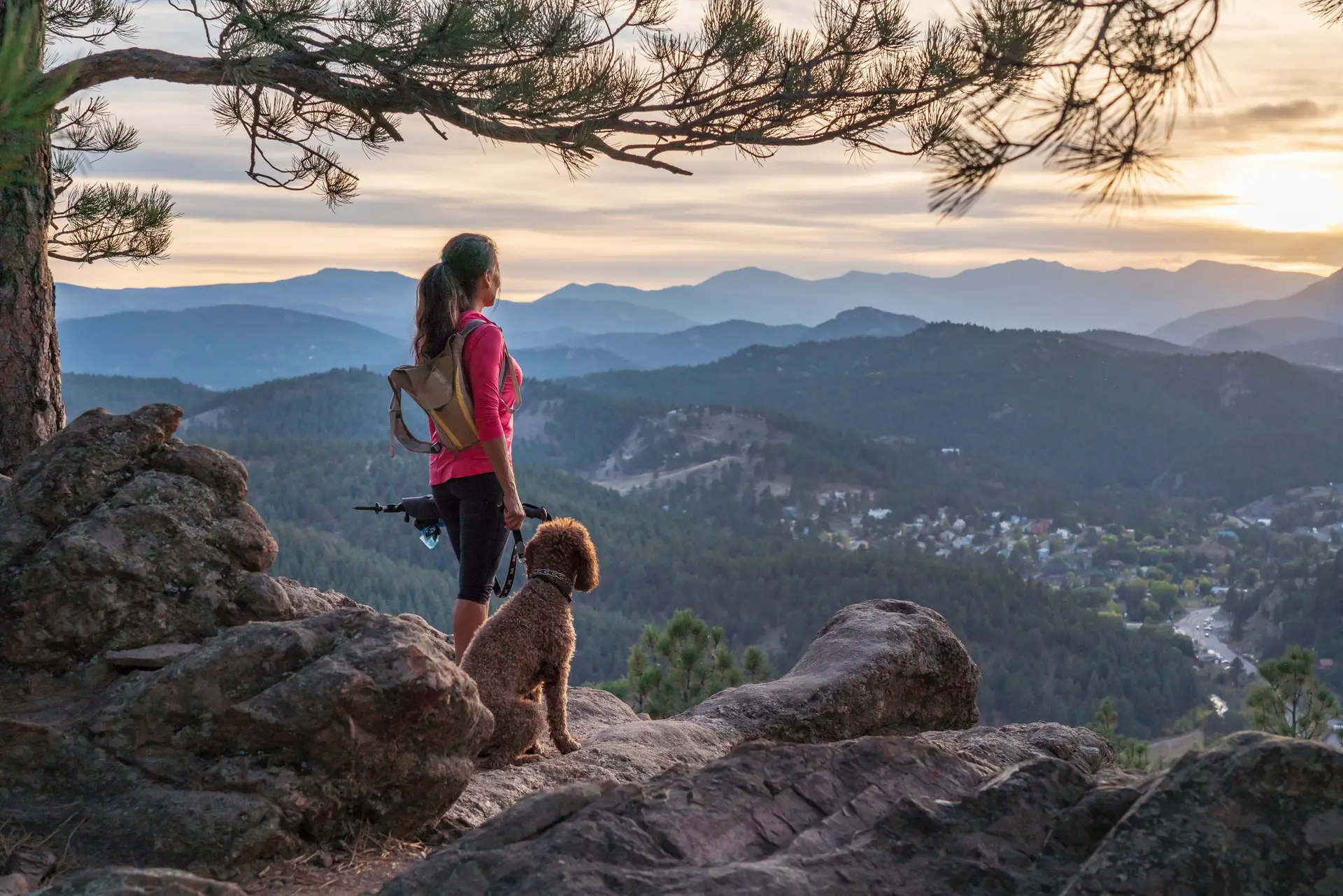 Woman hiking with her dog on a mountain trail at sunset near Denver, Colorado