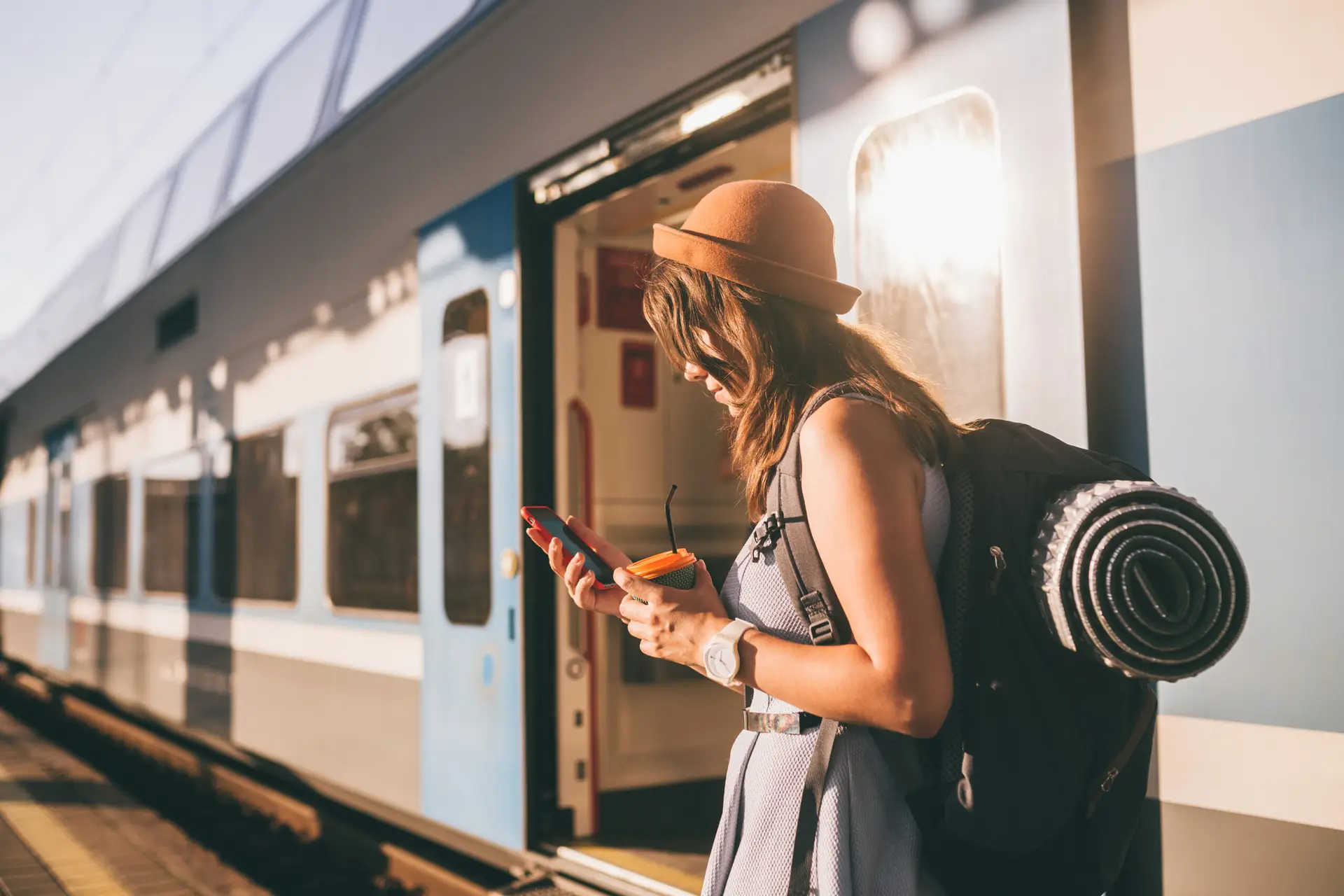 Young woman with backpack using phone near train platform