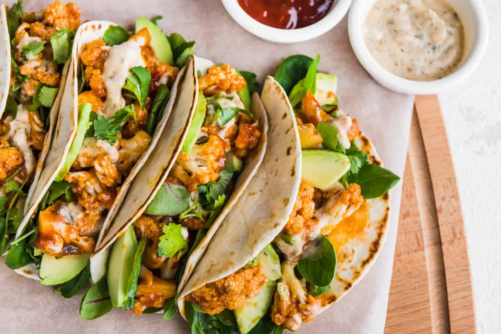 Vegan tacos with cauliflower, avocado and cilantro with sauces on a light background