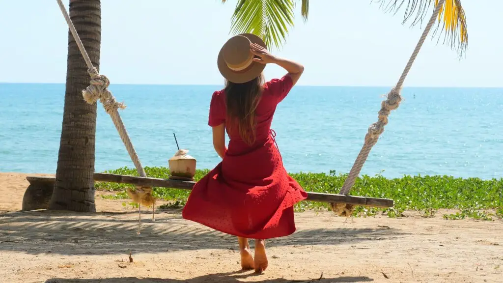 Solo female traveler on her swing sipping a cocktail looking at the beautiful ocean