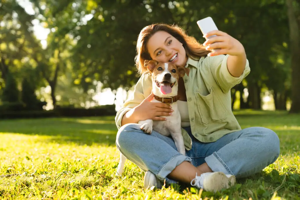 Woman traveling with her pet, a dog, and taking a selfie in a park
